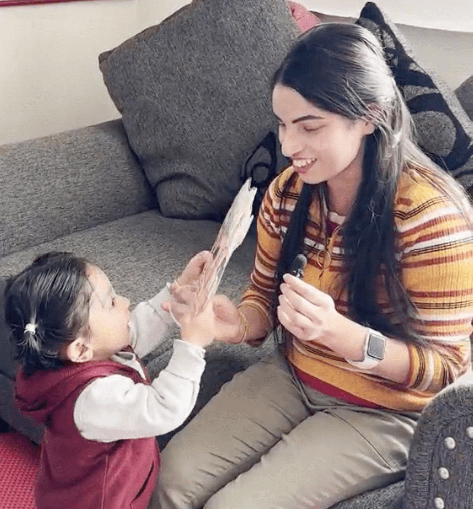 A Nepali mother and her toddler smile and engage with a toy during a Help Me Grow home visit in their living room.
